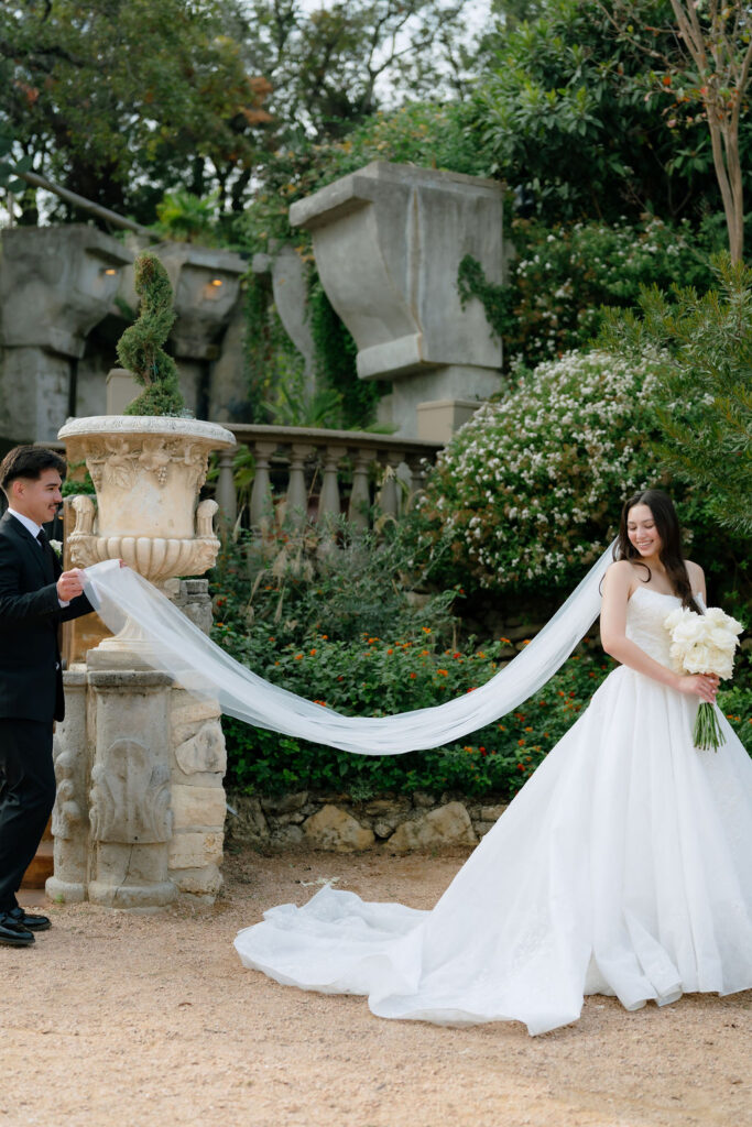 Groom carefully carrying bride's wedding gown between locations at Villa Antonia Jonestown Texas