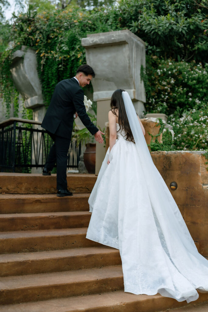 Groom carefully carrying bride's wedding gown between locations at Villa Antonia Jonestown Texas