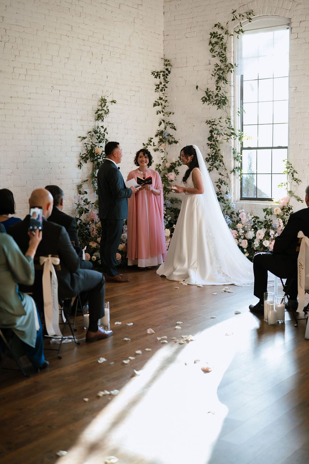Bride and groom exchanging vows during their winter wedding ceremony at One Eleven East in Hutto Texas, surrounded by lush floral arrangements, photographed by Andrea Jang Photography
