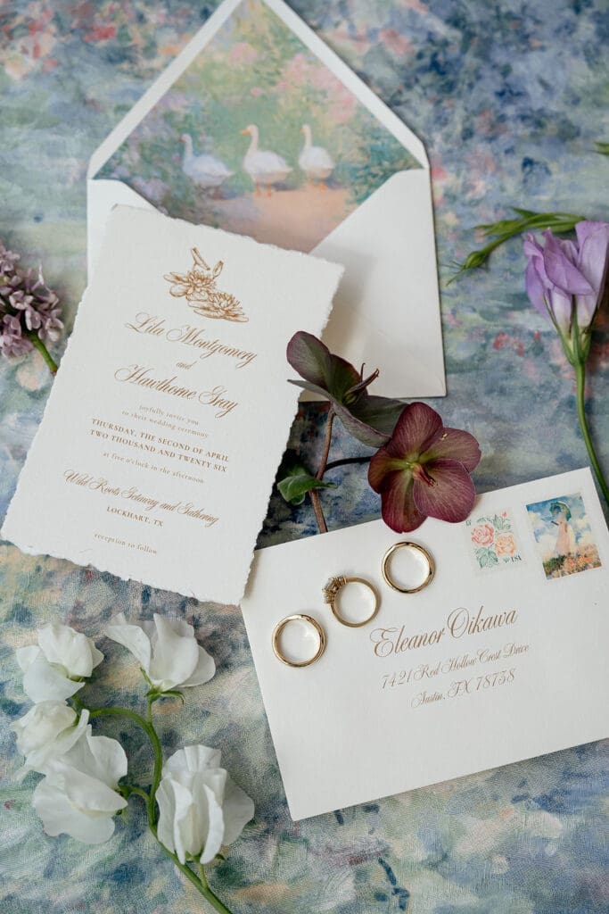 Monet inspired wedding invitation suite flat lay with watercolor envelope liner, wax seal, velvet ring boxes, and garden florals at Wild Roots Lockhart Texas by Austin wedding photographer Andrea Jang