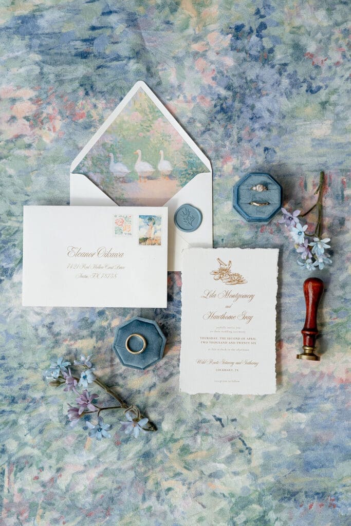 Monet inspired wedding invitation suite flat lay with watercolor envelope liner, wax seal, velvet ring boxes, and garden florals at Wild Roots Lockhart Texas by Austin wedding photographer Andrea Jang