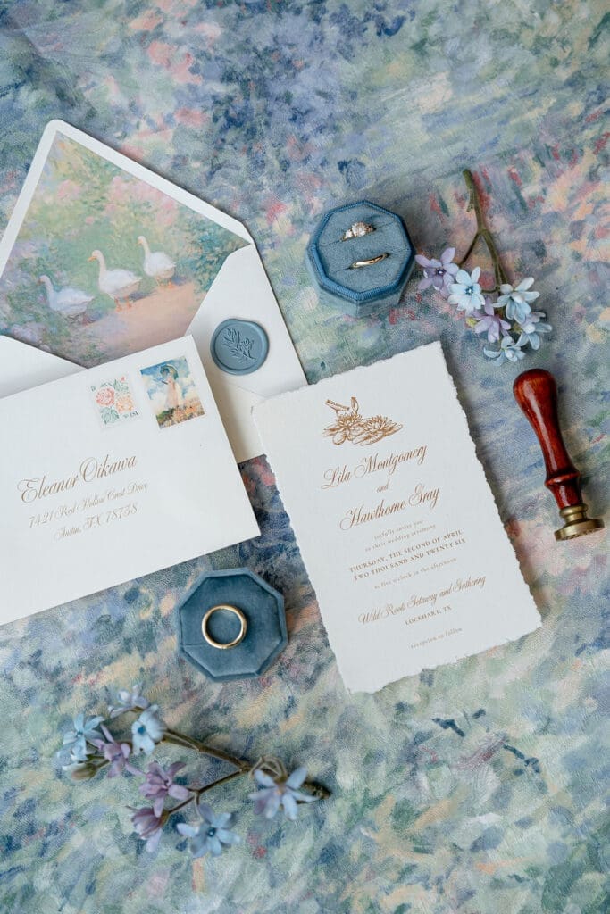 Monet inspired wedding invitation suite flat lay with watercolor envelope liner, wax seal, velvet ring boxes, and garden florals at Wild Roots Lockhart Texas by Austin wedding photographer Andrea Jang