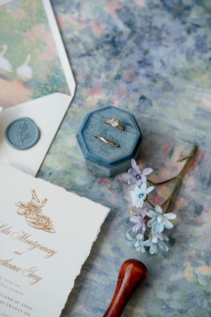 Monet inspired wedding invitation suite flat lay with watercolor envelope liner, wax seal, velvet ring boxes, and garden florals at Wild Roots Lockhart Texas by Austin wedding photographer Andrea Jang