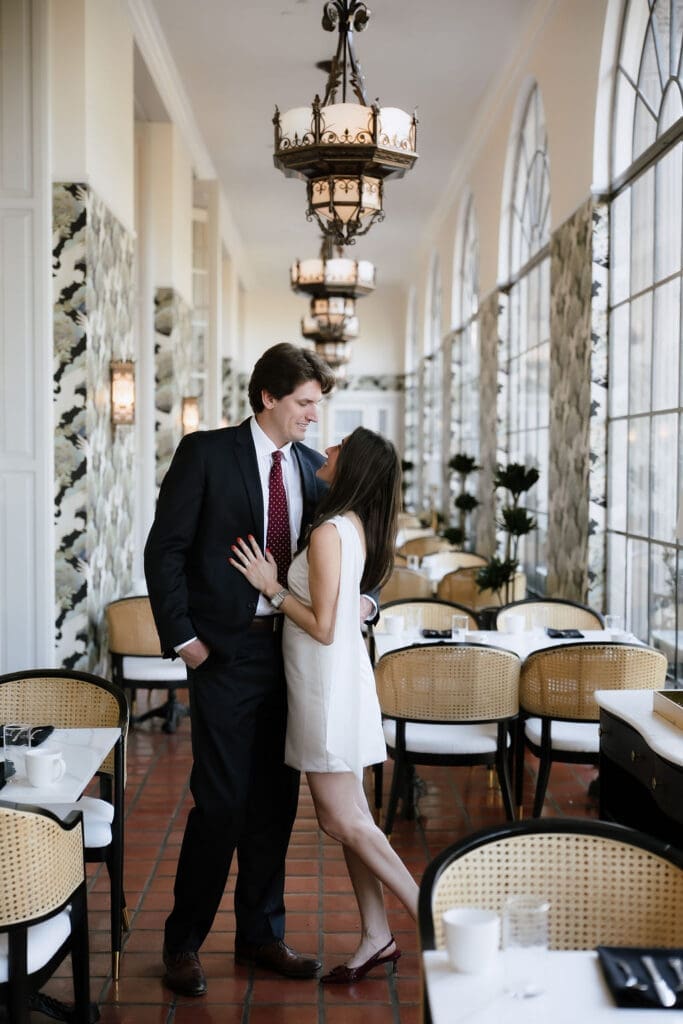 Engaged couple standing beneath ornate chandeliers in the marble lobby of the St. Anthony Hotel in San Antonio