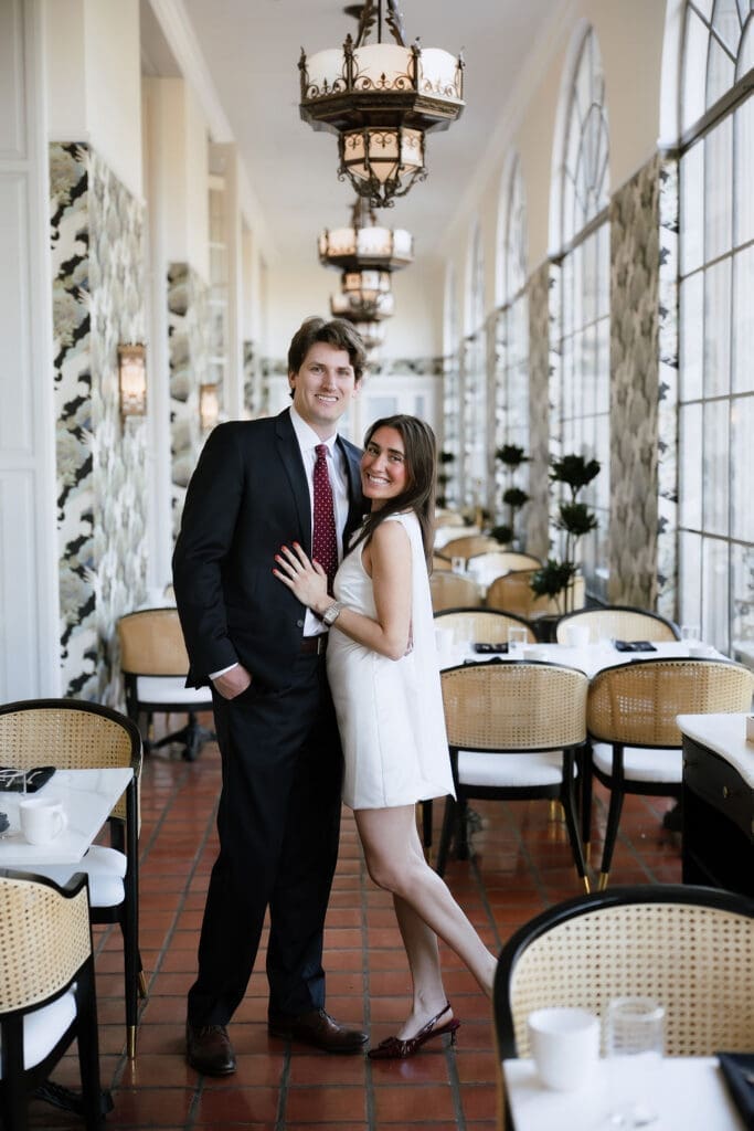 Engaged couple standing beneath ornate chandeliers in the marble lobby of the St. Anthony Hotel in San Antonio