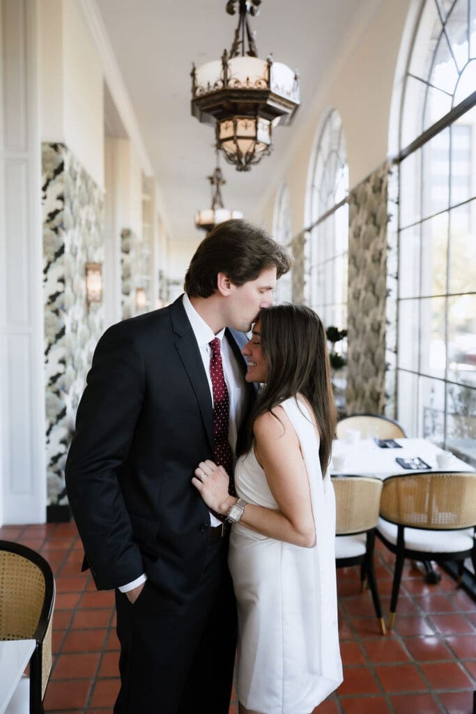 Engaged couple standing beneath ornate chandeliers in the marble lobby of the St. Anthony Hotel in San Antonio