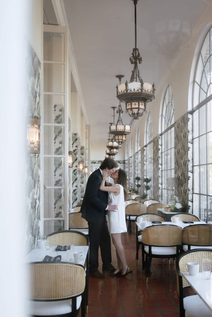 Engaged couple standing beneath ornate chandeliers in the marble lobby of the St. Anthony Hotel in San Antonio