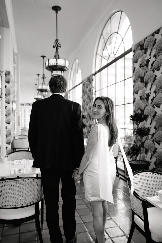 Engaged couple standing beneath ornate chandeliers in the marble lobby of the St. Anthony Hotel in San Antonio