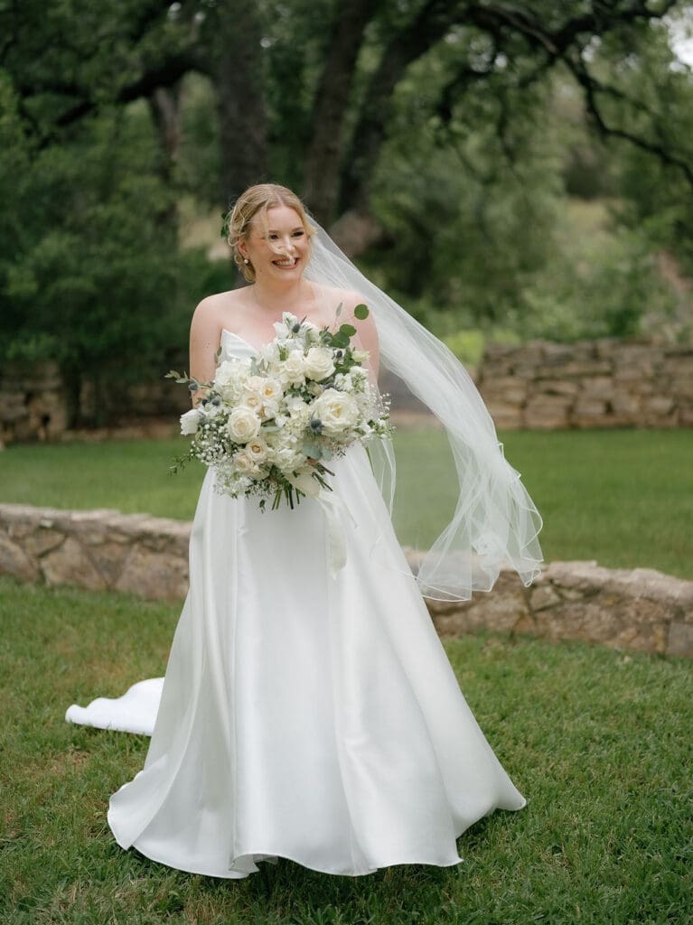 Dana standing alone in her wedding gown surrounded by soft greenery