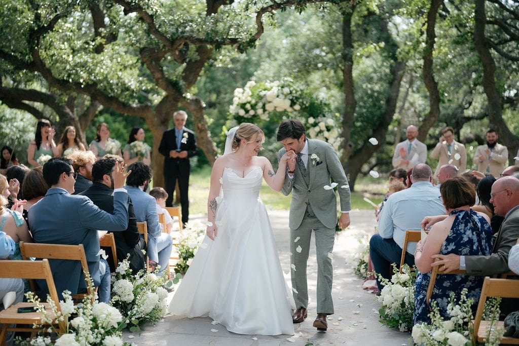 Newlyweds walking back up the aisle as guests cheer and applaud